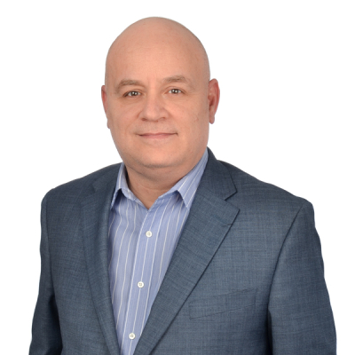 A middle-aged man with a bald head, wearing a blue suit jacket over a blue striped shirt, poses against a plain white background.