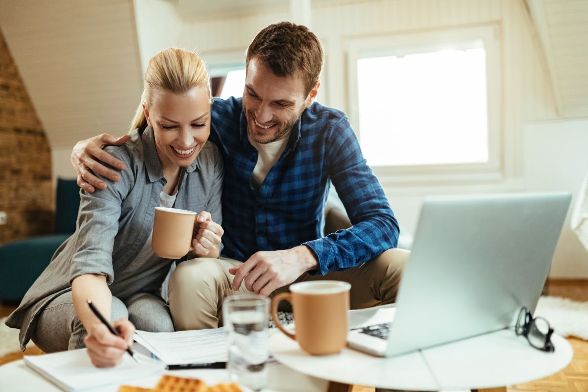 Two people smiling and drinking coffee while doing office work with laptop, pen and paper