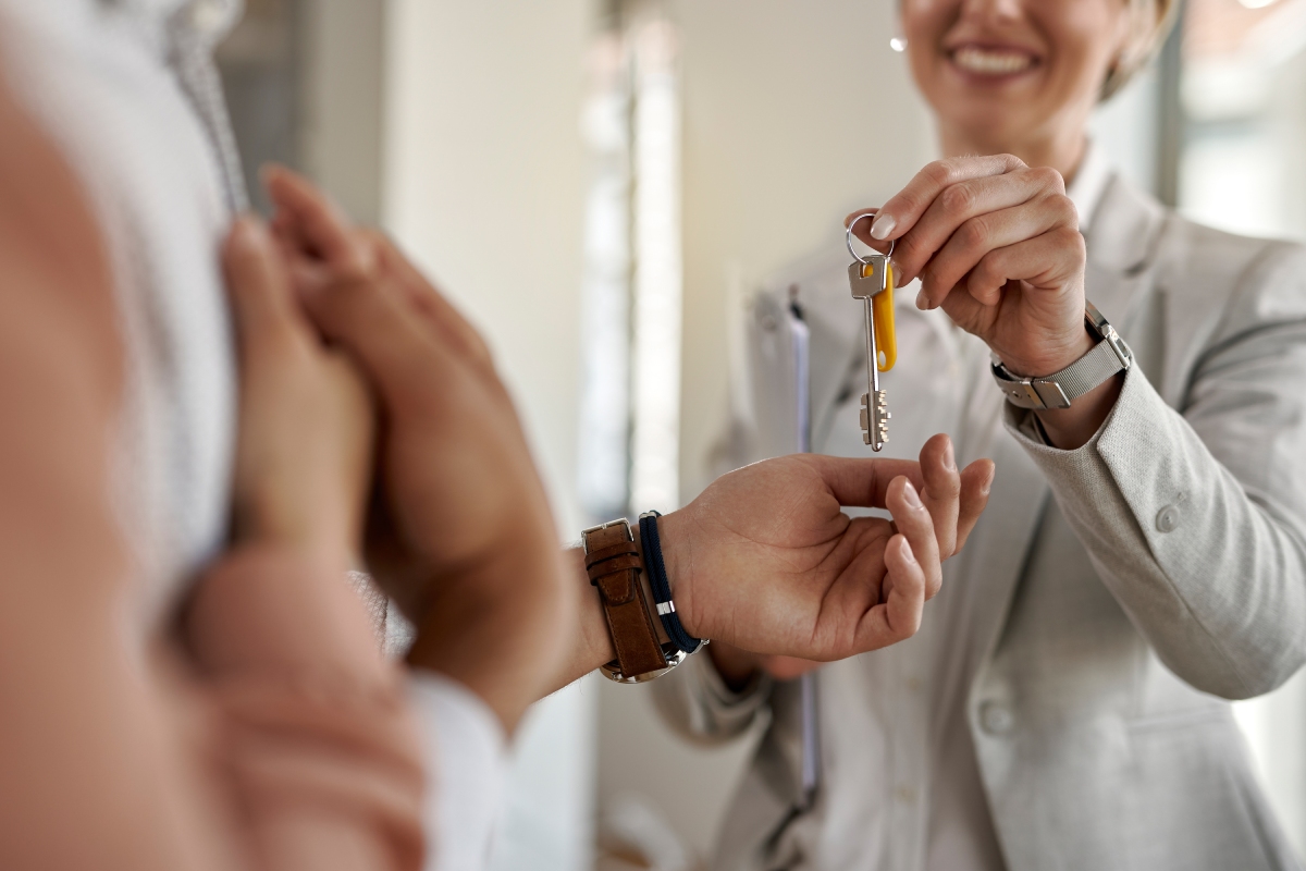 A person in a suit hands a set of house keys to another individual, symbolizing a real estate transaction or new home ownership.