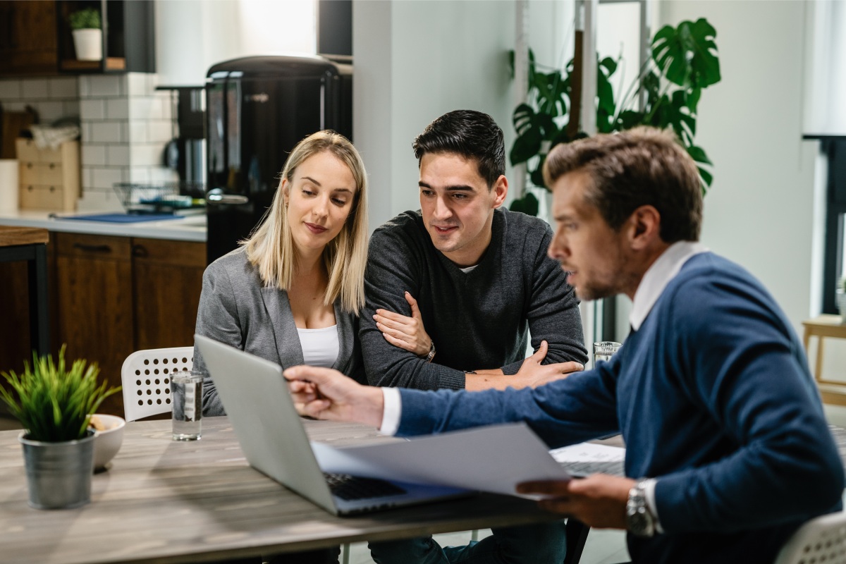 A financial advisor points to a laptop screen while explaining how to access home equity through refinancing to a couple seated at a table.